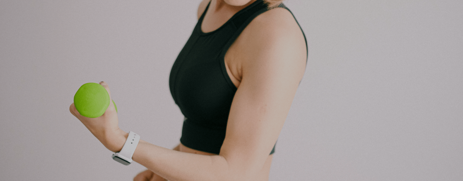 Woman exercising with a green ball, wearing a black sports top and white smartwatch. Focus on fitness and wellness.