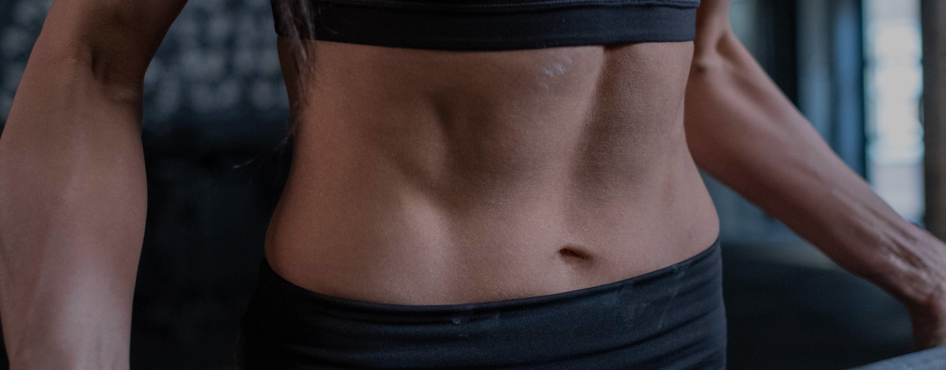 Close-up of a woman's toned midriff wearing a black sports bra, highlighting fitness and active lifestyle.