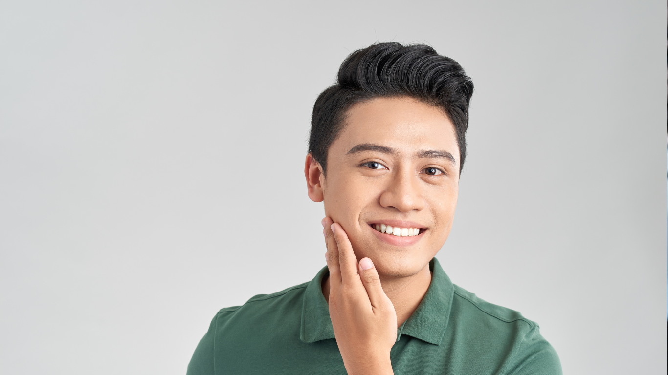 Smiling person touching smooth cheek, showcasing skincare or collagen supplement benefits. Wearing a green shirt, against a neutral background.
