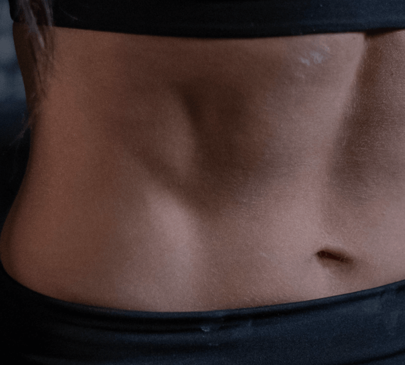 Close-up of a toned abdomen in a black workout outfit, illustrating fitness and wellness benefits, possibly related to collagen supplements.