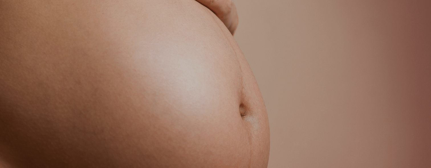 Close-up of a pregnant belly with smooth skin on a neutral background, highlighting skin health and wellness.