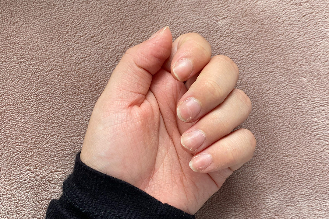 Close-up of a hand with natural, short nails against a textured beige background, focusing on nail health and beauty.