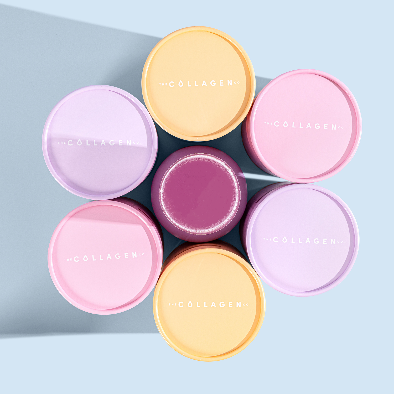 Colorful collagen containers arranged in a floral pattern on a light blue background, emphasizing beauty and skincare supplements.