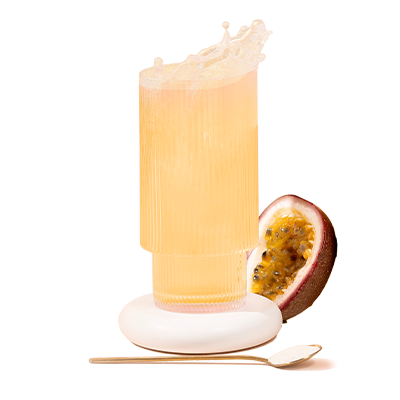 Tall glass of peach-colored collagen drink with a passion fruit half and a small spoon on a white coaster.