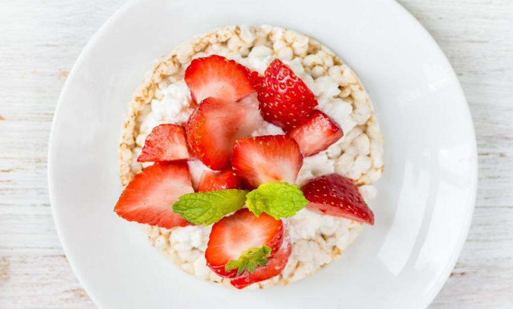 Rice cake topped with cottage cheese, fresh strawberry slices, and mint on a white plate.