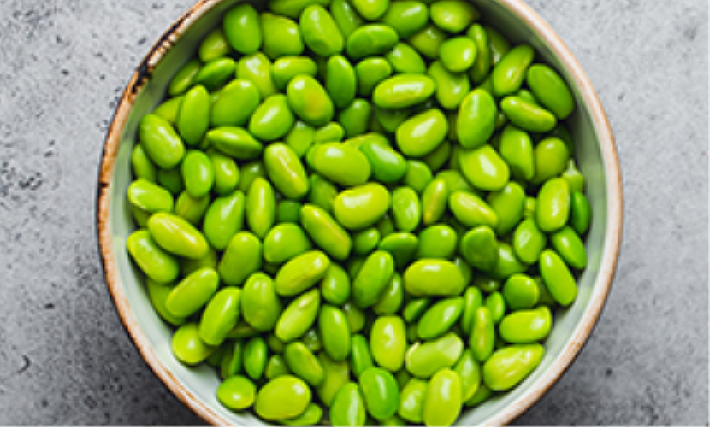 Bowl of vibrant green edamame beans on a textured gray surface.