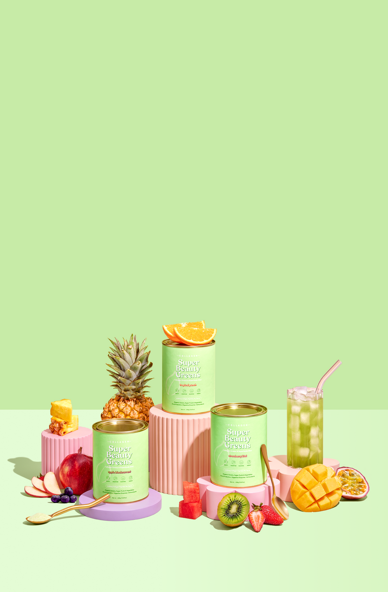 Colorful display of Super Beauty Greens collagen containers surrounded by fresh fruit, including pineapple, kiwi, mango, and a refreshing drink.