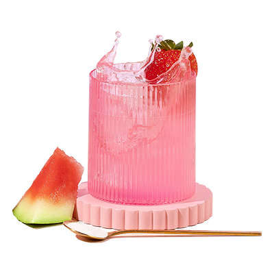 Pink collagen drink splashes in a ribbed glass, garnished with a strawberry. Slices of watermelon and a gold spoon nearby on a pink coaster.