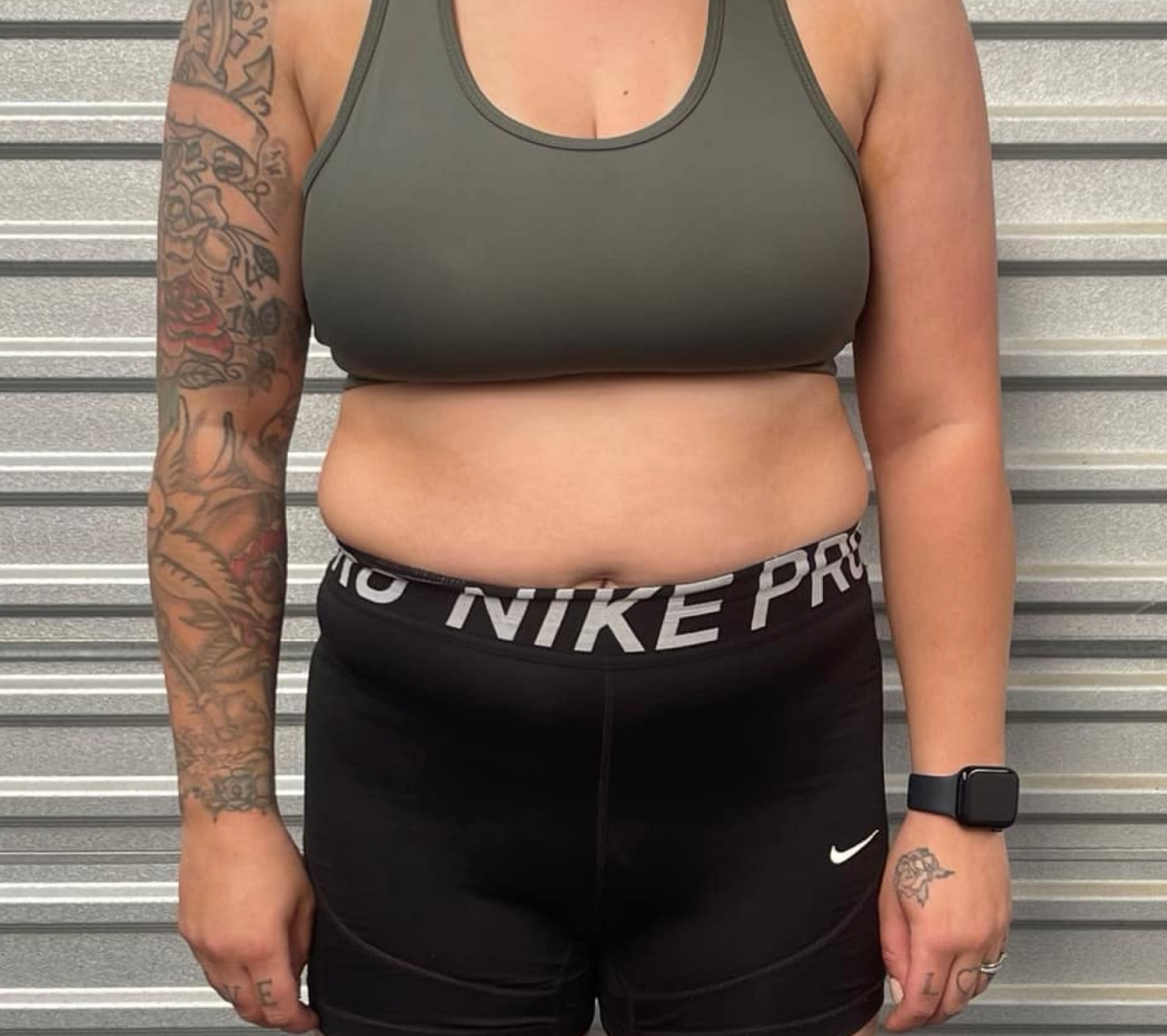 Person in workout attire, standing in front of a corrugated metal background, showcasing fitness progress.