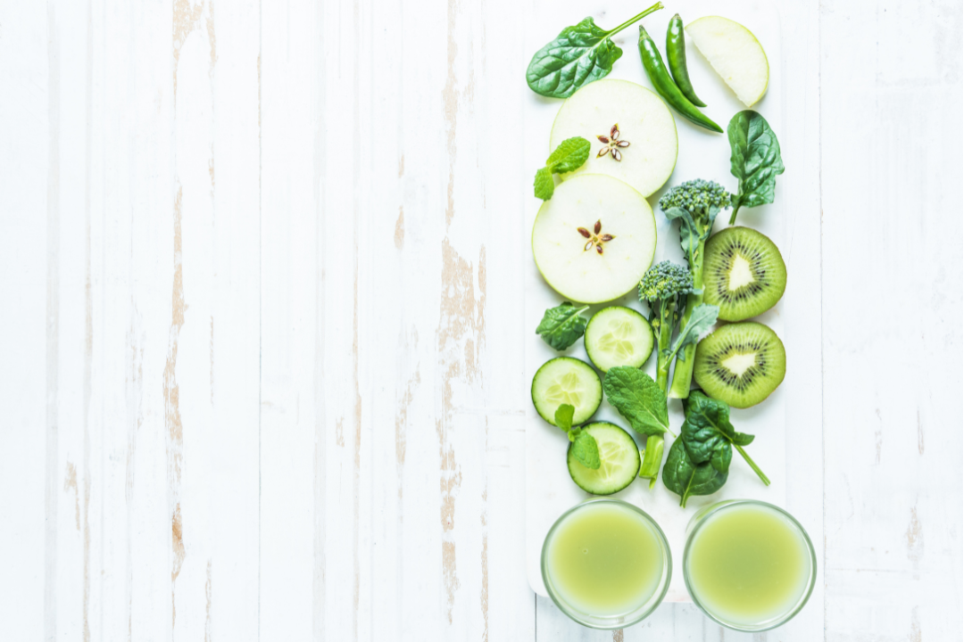 Sliced green fruits and vegetables with two glasses of green juice on white wooden table, promoting collagen supplements and natural beauty wellness.