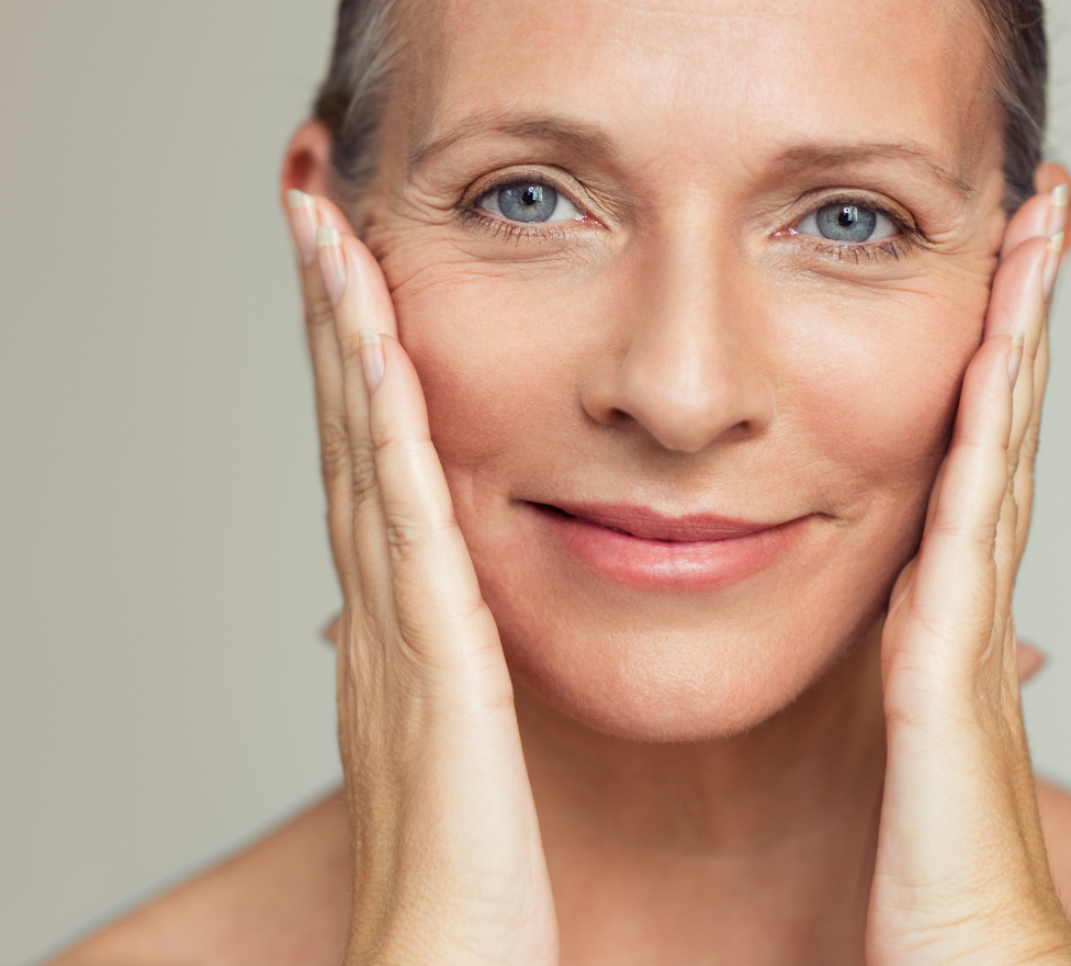 Middle-aged woman touching her face with both hands, showcasing smooth skin and a serene expression, emphasizing beauty and skincare benefits.