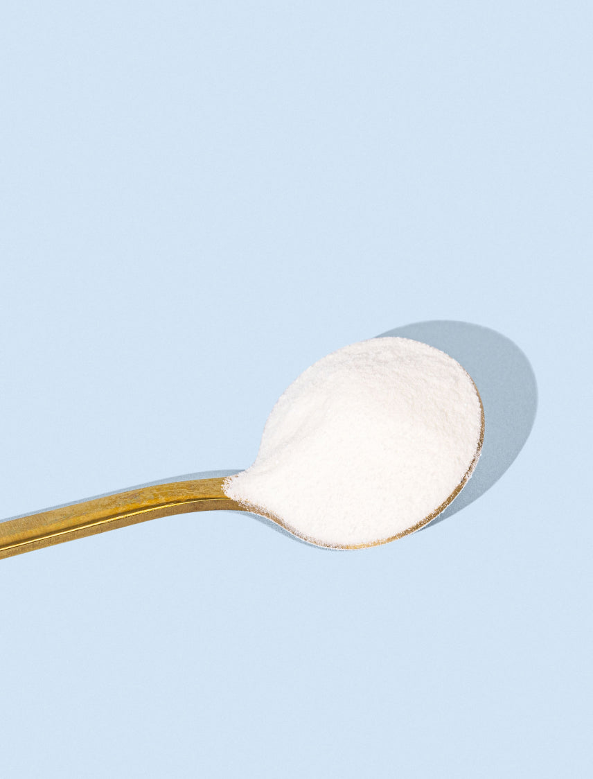 Gold spoon filled with white collagen powder on a light blue background, emphasizing beauty and supplement benefits.