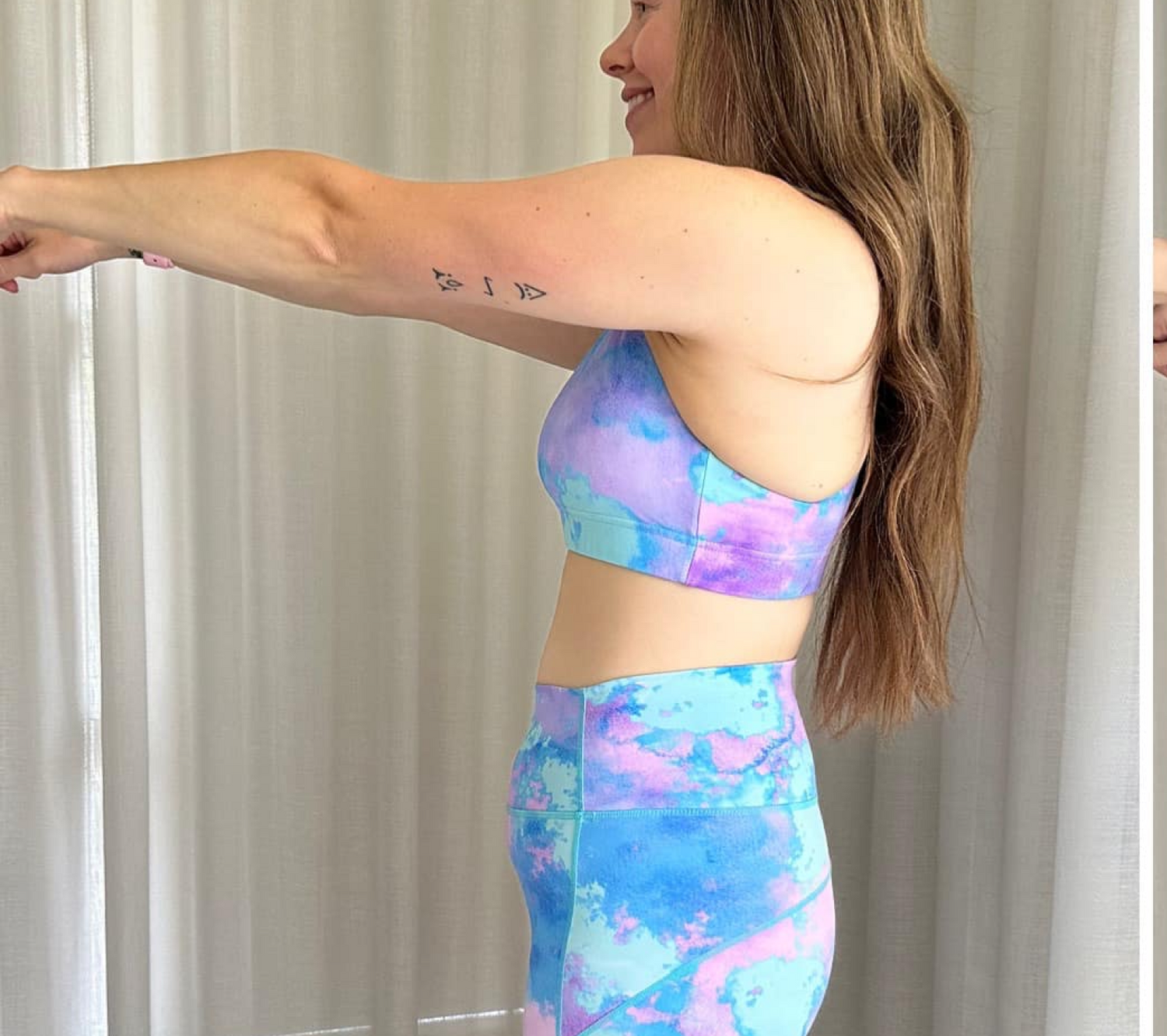 Person in vibrant blue and purple tie-dye workout set, showing a tattoo on their arm, against a light curtain backdrop.