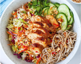 A vibrant bowl with grilled chicken, soba noodles, sliced cucumber, mixed veggies, and peanuts, highlighting fresh, healthy ingredients.