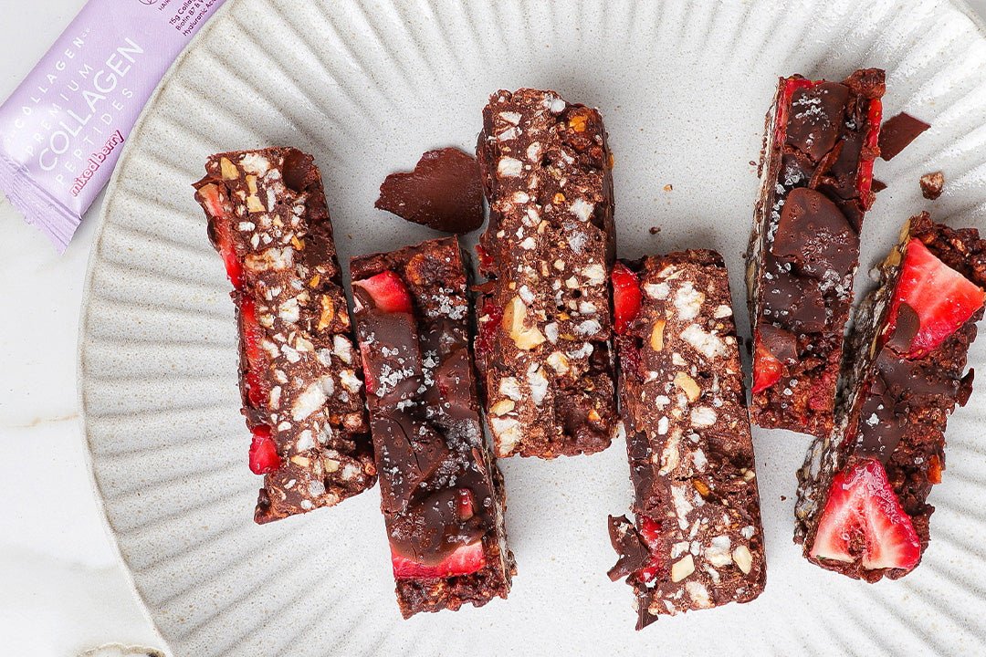 Chocolate strawberry collagen bars topped with nuts and seeds on a ribbed plate. A collagen packet is partially visible in the corner.