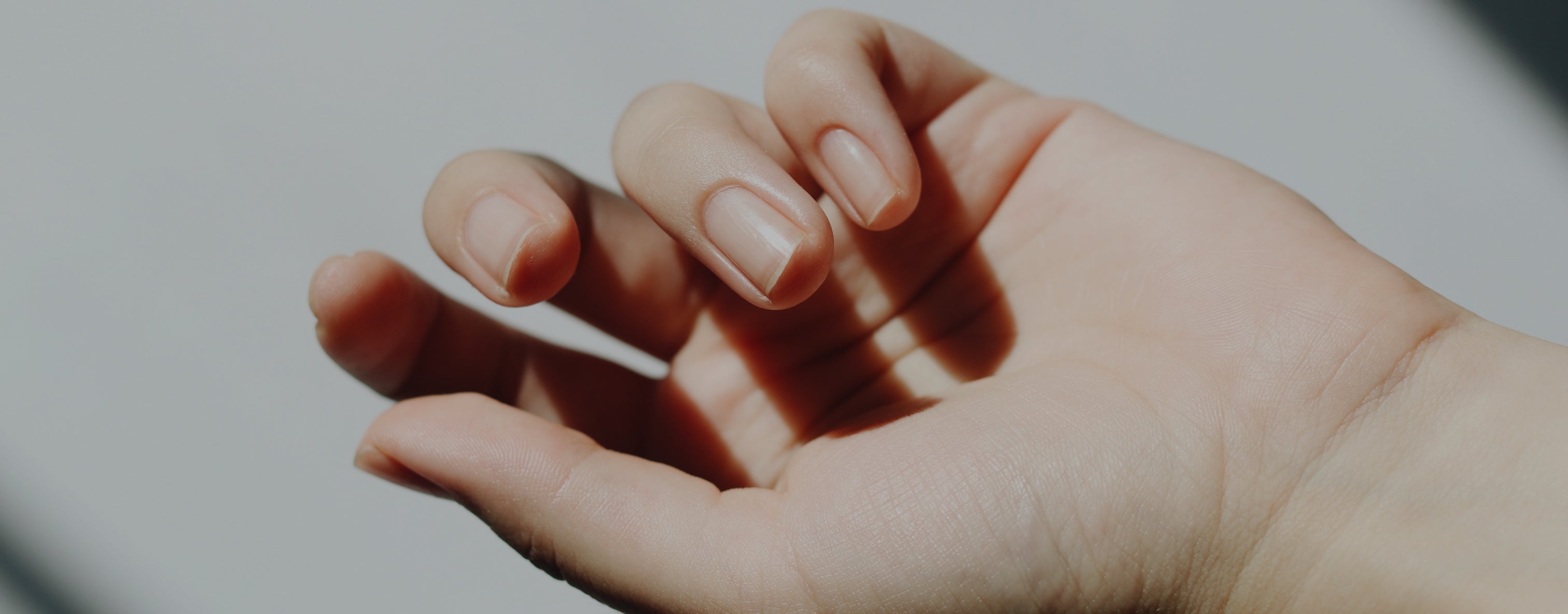 Close-up of a hand with natural nails gently curved, highlighted by soft lighting. Perfect for skincare, beauty, and collagen supplement themes.
