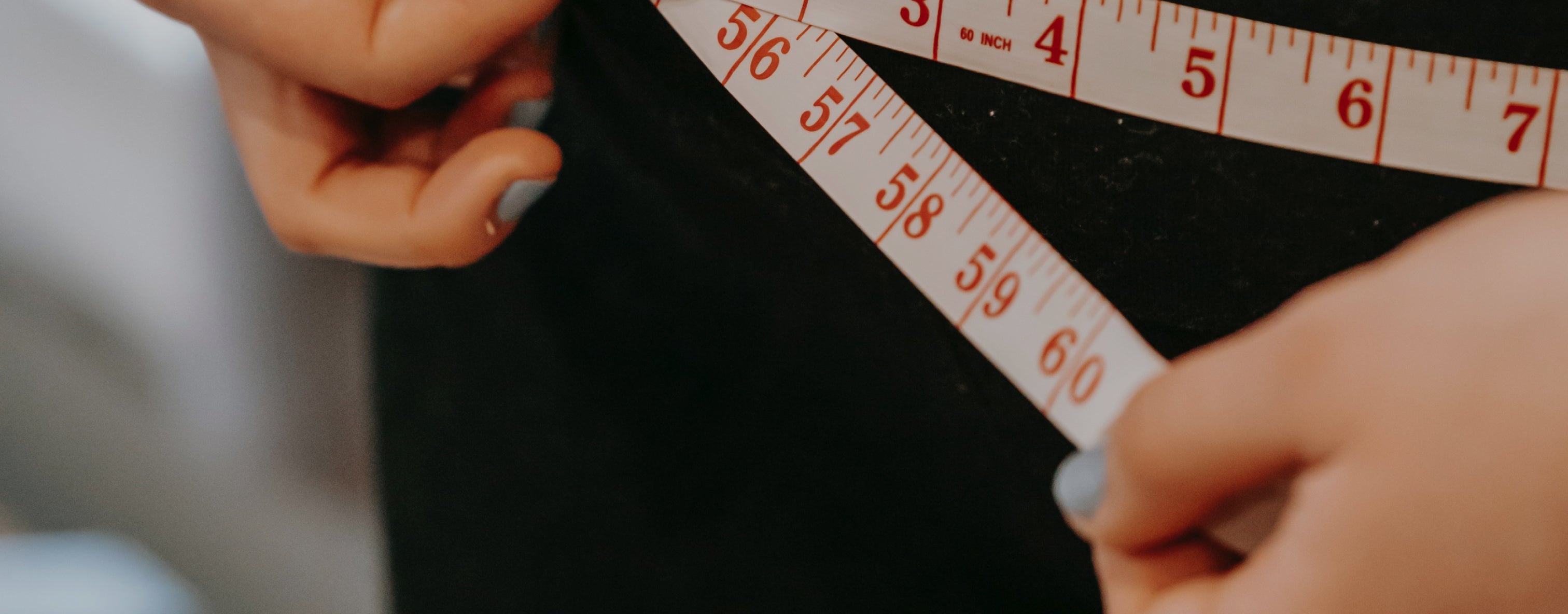 Hands using a measuring tape to check waist size, suggesting fitness or wellness focus. Nails are painted light blue.
