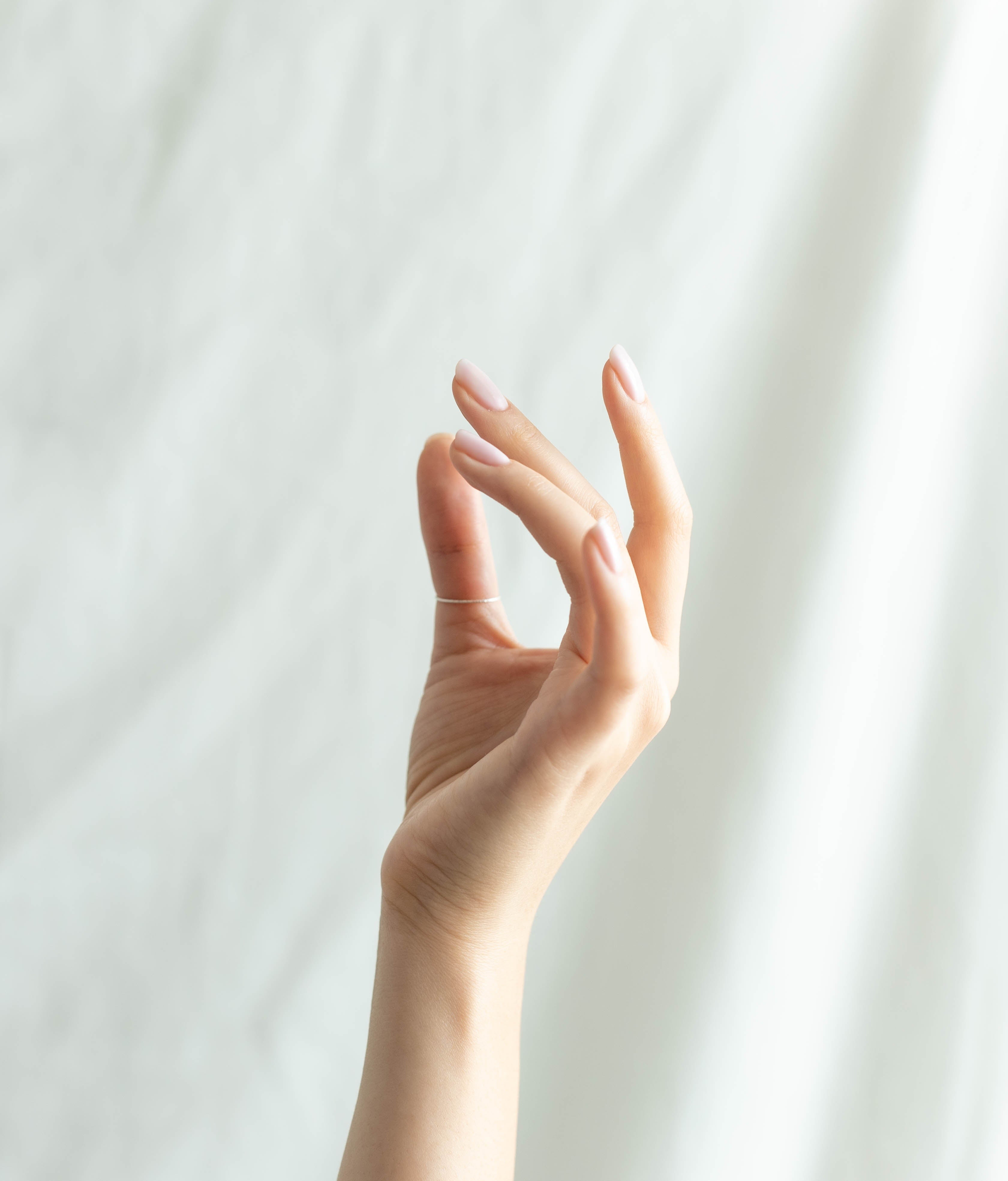 A graceful hand with natural nails, slightly curved fingers, against a soft white background, highlighting skin beauty and elegance.