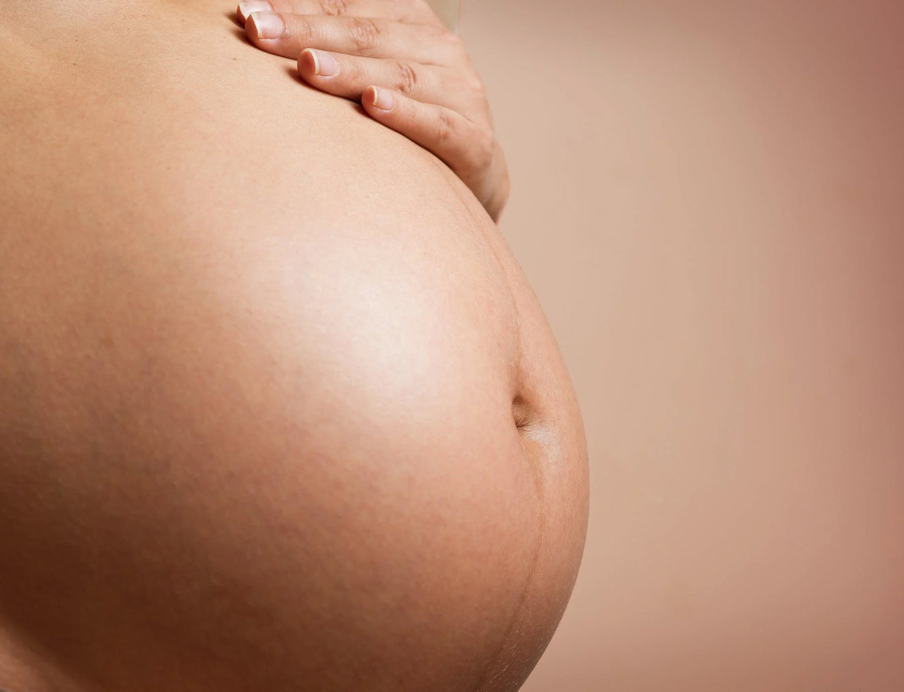 Close-up of a pregnant belly with a hand resting on top, emphasizing natural beauty and wellness.