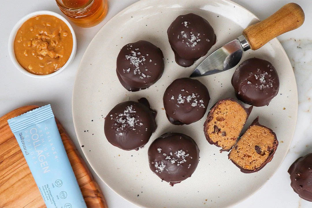 Plate of chocolate-covered collagen protein balls, one cut open, with a knife. Peanut butter and a collagen supplement packet nearby.