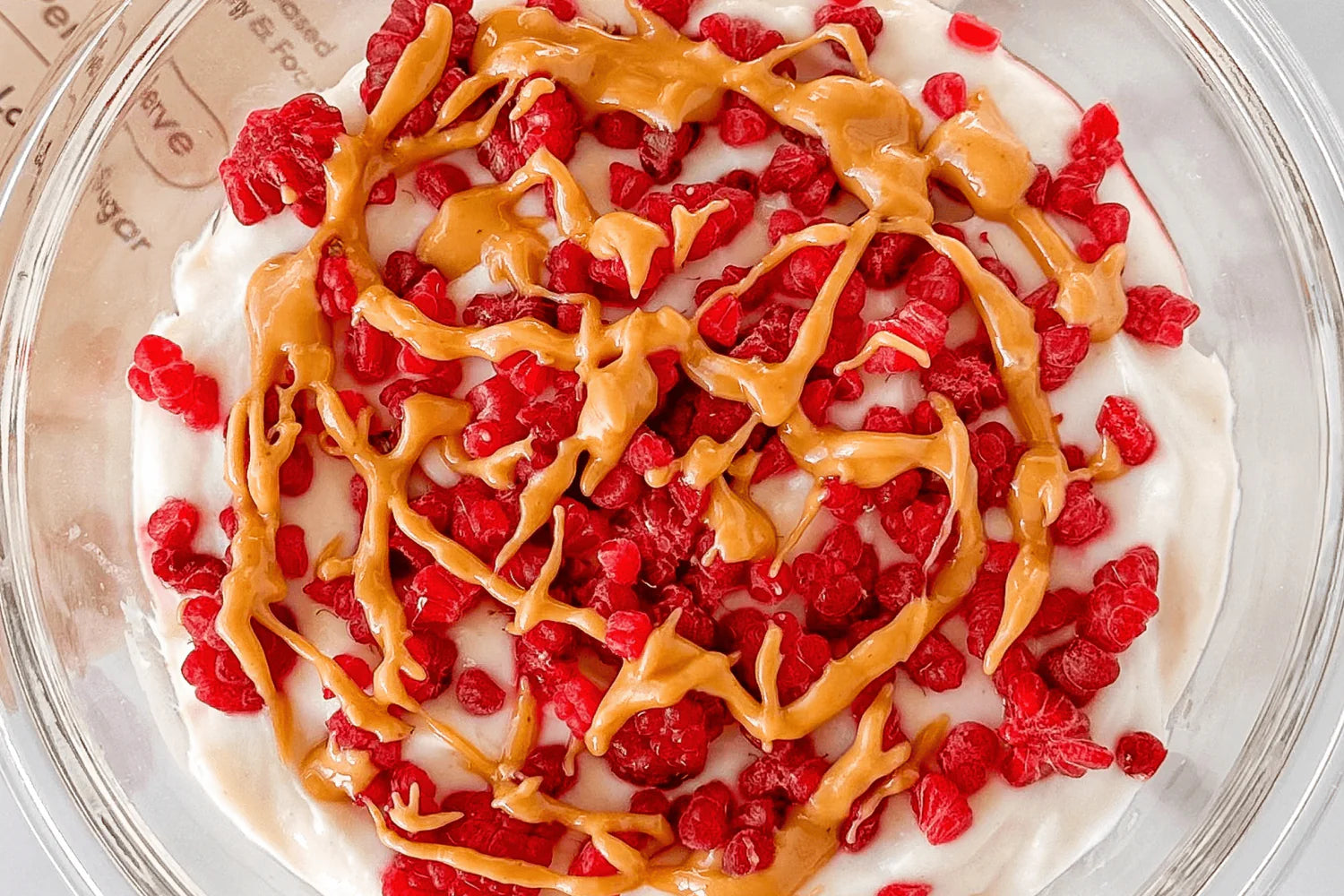 Bowl with creamy yogurt topped with vibrant red berries and a rich drizzle of peanut butter.