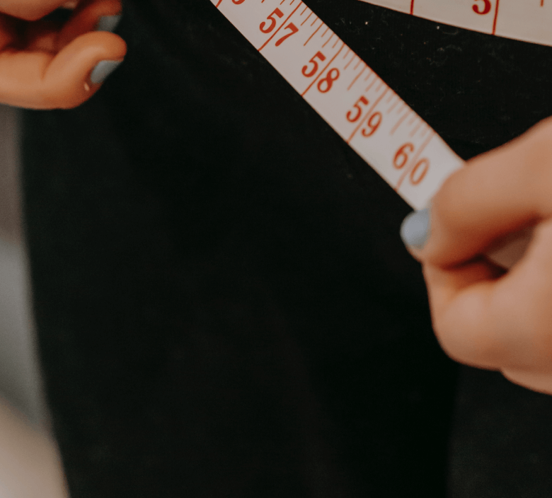 Close-up of hands measuring waist with a tape measure, indicating health or fitness tracking.