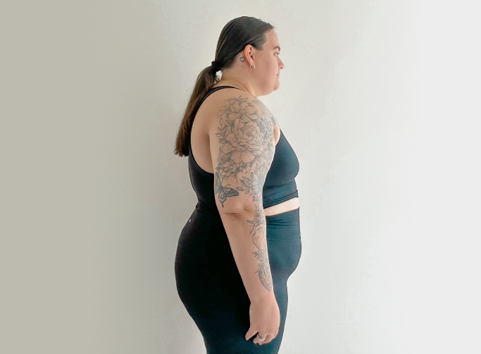 Person in black activewear standing sideways, showcasing a floral arm tattoo, against a plain background.