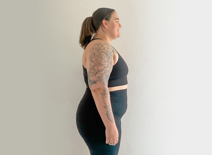 Profile of a woman in workout attire with floral arm tattoos, standing against a neutral background.